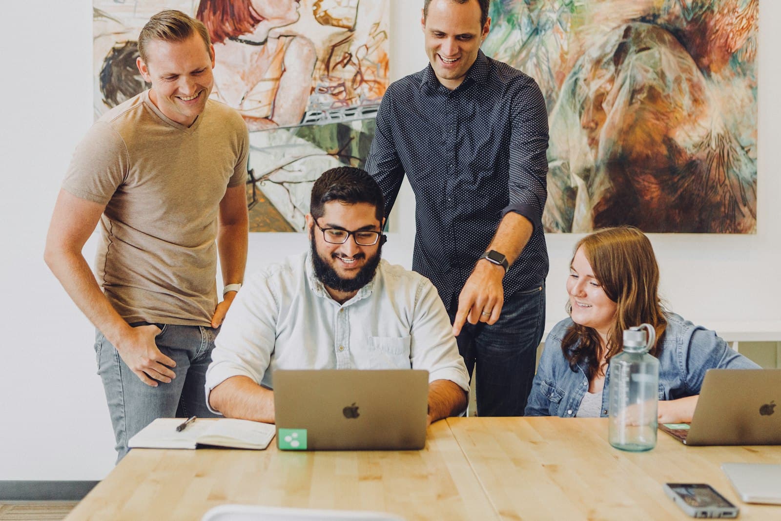 Four colleagues laughing around a laptop during a design review